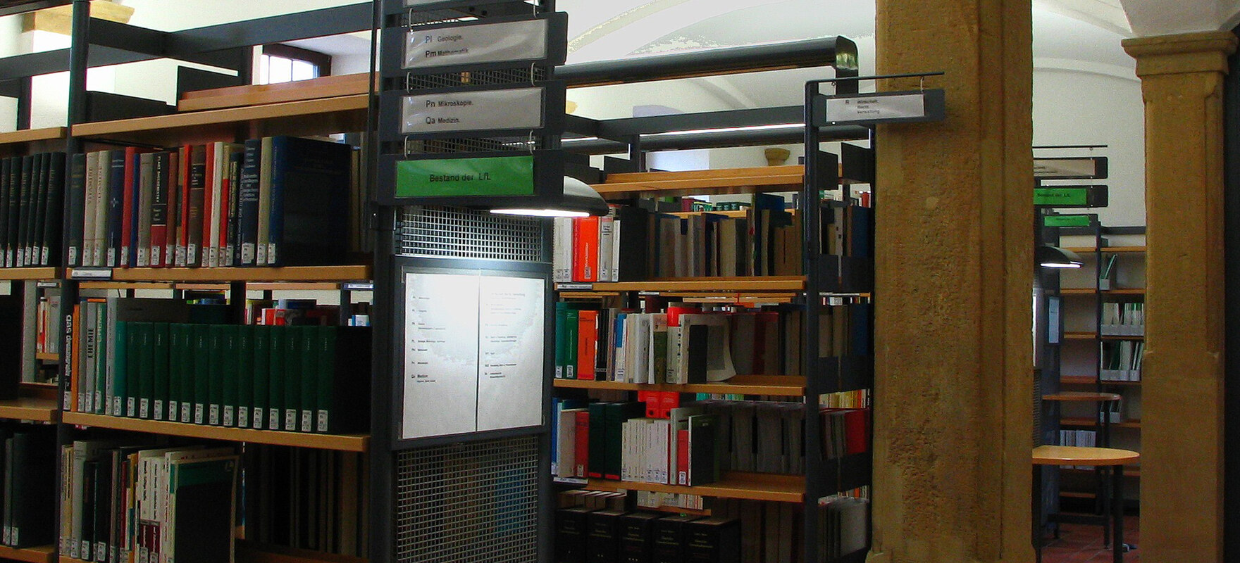 Einblick in die Bibliothek mit beschrifteten Bücherregalen aus Metall und Holz.