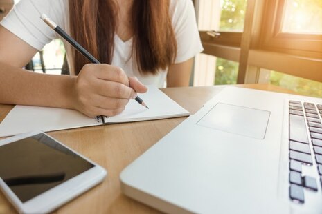 Junge Frau sitzt am tisch vor ihrem Laptop und füllt Bewerbungsformular aus.