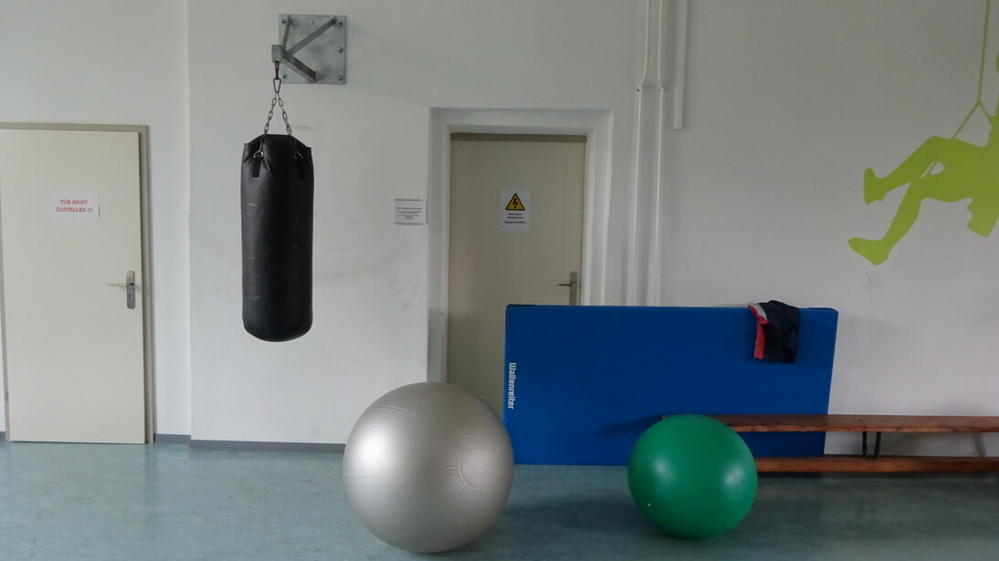 Ein großer Boxsack hängt von der Decke. Im Vordergrung sind große Gymnastikbälle zu sehen.