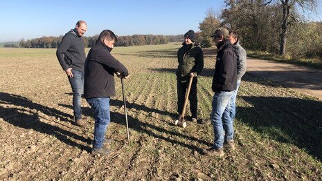 Fünf Personen stehen mit einem Bohrstock auf einem Feld
