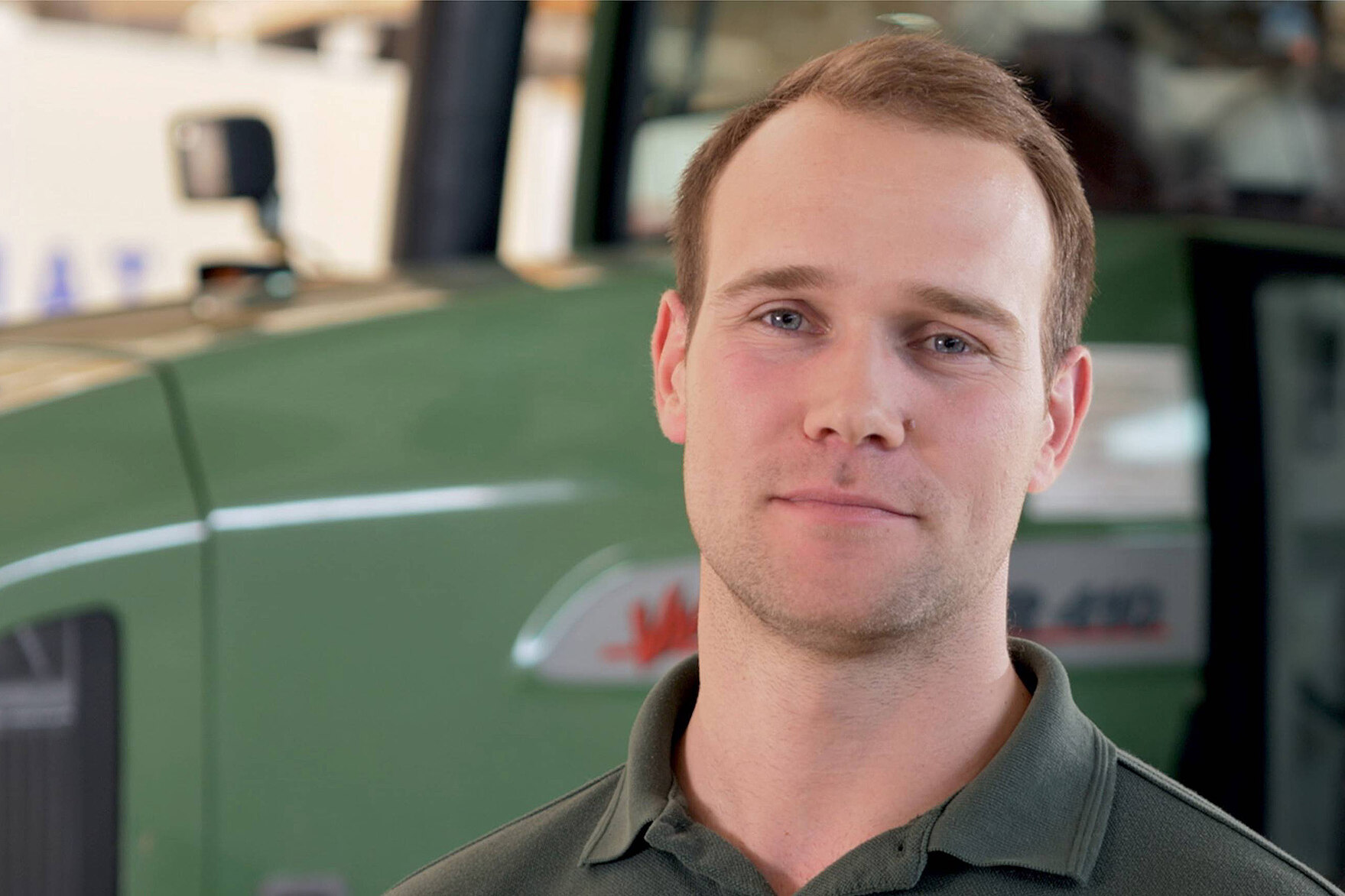 Landwirt steht vor einem Traktor und lächelt in die Kamera.